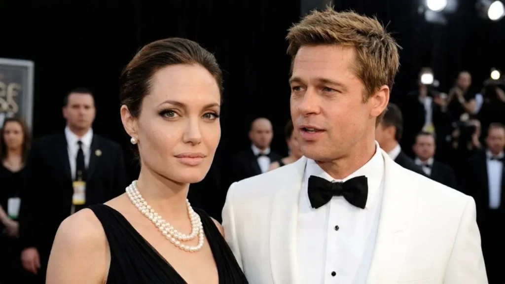 Angelina Jolie posing elegantly in a black designer gown at a recent Paris film premiere, looking deeply reflective under glowing theater lights.