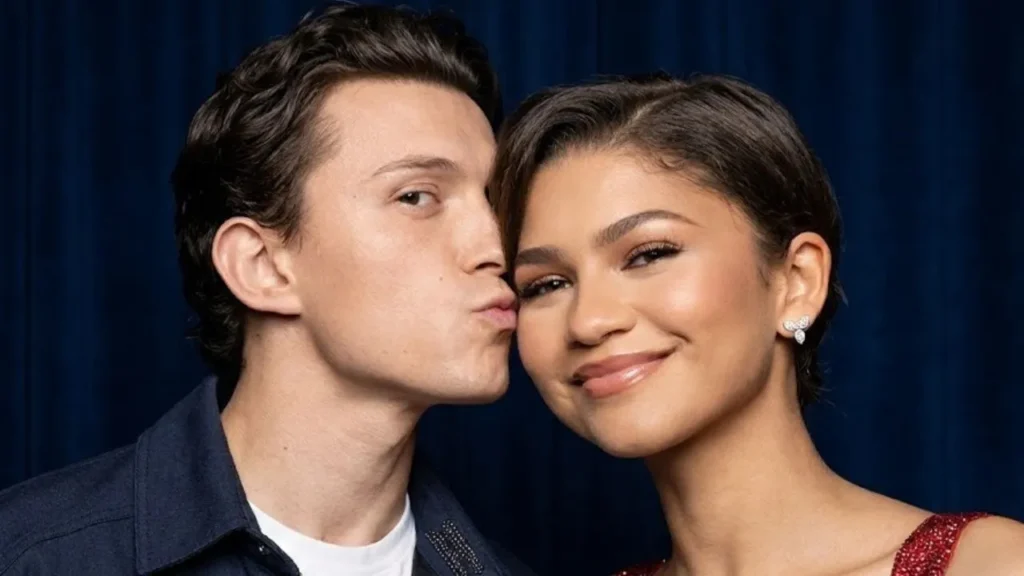 Zendaya smiling in a red and blue sparkly Versace outfit while Tom Holland kisses her head during their Rome press tour stop.