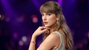 A professional 4K editorial portrait of Taylor Swift looking over her shoulder from a side-profile angle. She is wearing a pale sage-green velvet corset gown with intricate metallic beadwork and fringe, featuring her signature bangs, red lipstick, and elegant jewelry. The background is softly blurred with purple and pink bokeh lights.