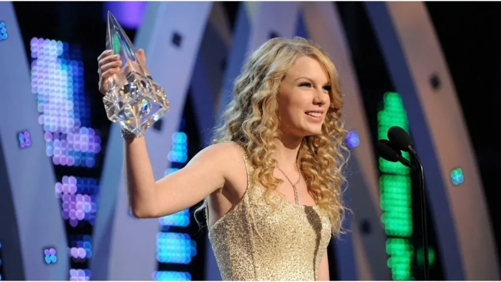 Taylor Swift performing with an acoustic guitar under golden stage lighting at a country music celebration