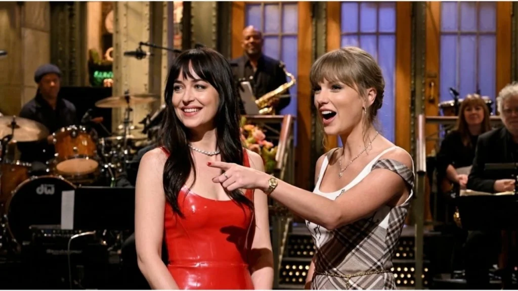 Taylor Swift and Dakota Johnson smiling together during Saturday Night Live monologue studio performance