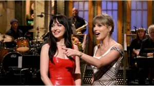 Taylor Swift and Dakota Johnson smiling together during Saturday Night Live monologue studio performance